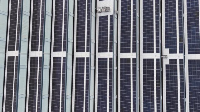 4k Aerial view solar panel facade on modern high rise with bright sun flare, glass and metal surfaces, strong geometric lines, clean energy architecture