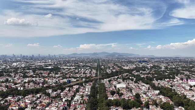 Aerial panoramic view of a vast urban landscape crossed by a straight avenue and power lines toward a distant skyline in Mexico City, Mexico