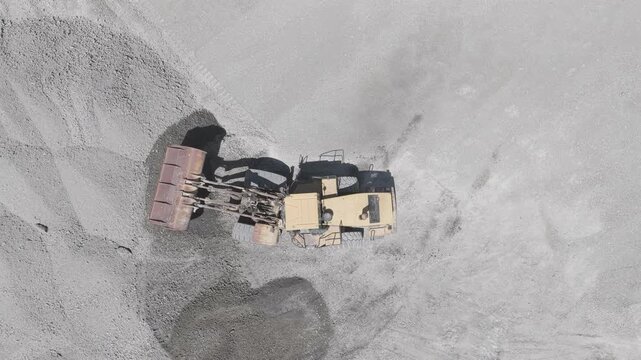 Top-down aerial view of a wheel loader pushing gravel in a sand and gravel quarry while the camera hovers overhead, D-Log M