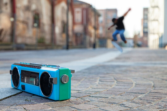 Colorful boombox on pavement playing music on a street while skateboarder performs trick
