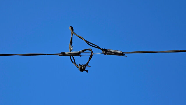 Spliced electrical telecommunication cable with tension clamps and knotted wire hanging against a clear blue sky