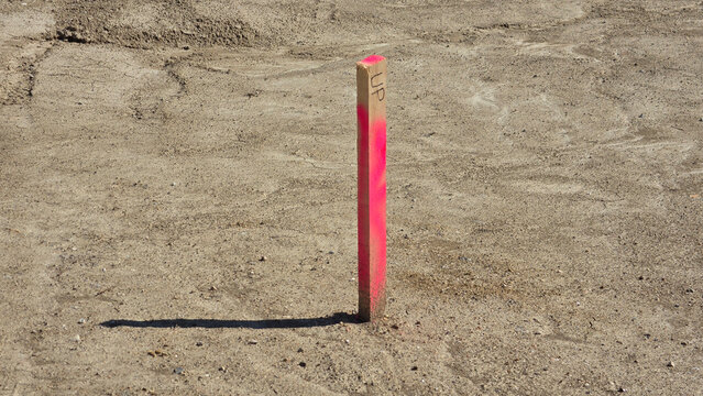 Wooden construction survey stake painted neon pink driven into dry barren dirt ground with hard shadows