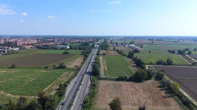 Aerial View of a Highway Through Rural Landscape: An expansive aerial shot reveals a long, straight highway cutting through cultivated fields and distant town, under a clear blue sky.