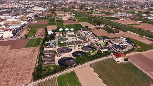 Aerial view of a modern wastewater treatment plant featuring circular clarifiers, aeration basins with activated sludge, biogas digesters, and solar panels surrounded by agricultural fields
