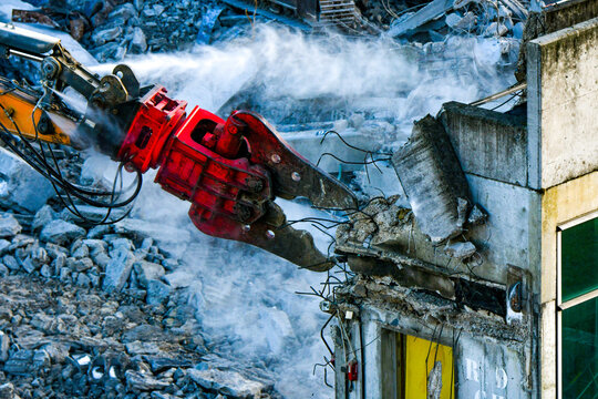 Pince hydraulique de d&eacute;molition rouge d&eacute;coupant les armatures en b&eacute;ton d'un b&acirc;timent en ruine, jet d'eau anti-poussi&egrave;re