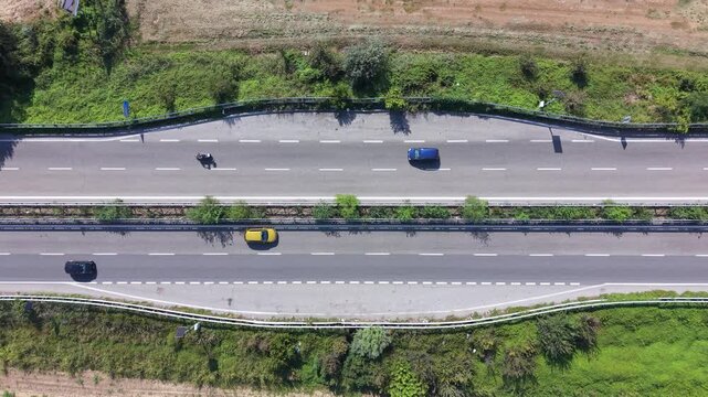Aerial View Highway. An overhead drone shot captures the flow of traffic on a modern highway, with cars and a motorcycle navigating the lanes amidst green verges and agricultural fields.