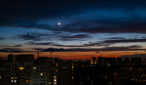 crescent moon over city skyline at twilight panoramic view, urban night landscape with building silhouettes and glowing horizon, scenic city sunset with crescent moon and Construction cranes