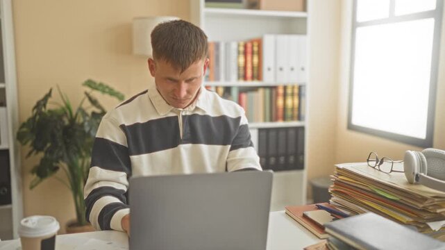 Young caucasian man student holding face with hand beside laptop amid books, folders and coffee cup in home office study; stress concentration.