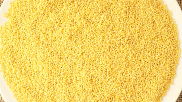 Raw yellow hulled millet rotating on a white background