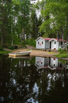 Zwei Holzh&uuml;tten und ein Ruderboot am Ufer eines Sees in Mitten von Wald. Idylle pur in Schweden.