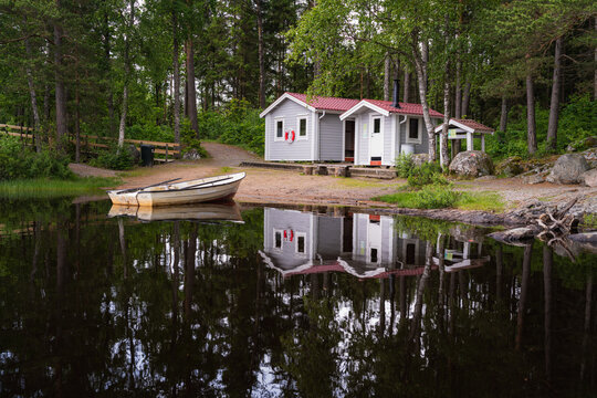 Zwei Holzh&uuml;tten und ein Ruderboot am Ufer eines Sees in Mitten von Wald. Idylle pur in Schweden.