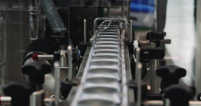 Empty soft drink cans advance along narrow conveyor toward processing equipment. Automated guides control spacing directing containers through packaging line