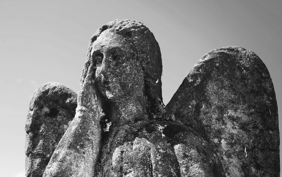Ancient weathered stone angel statue in black and white, symbolizing grief, mourning, remembrance, faith, death and eternal life.