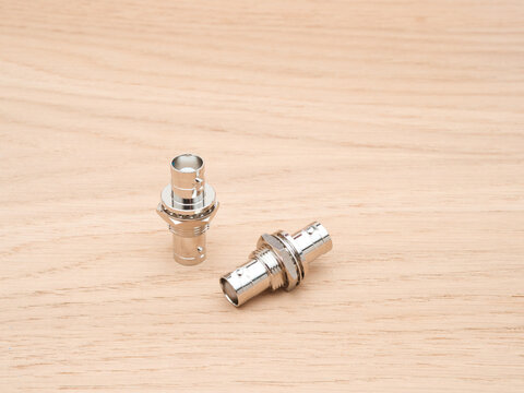 Two Silver BNC Connectors on Wood - Two shiny silver BNC connectors are arranged on a light-colored wooden surface, showcasing their design and metallic luster.