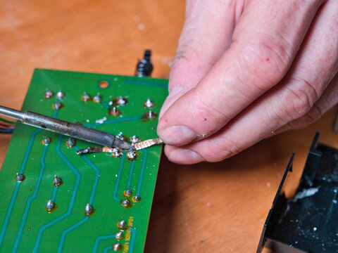 Desoldering Electronic Circuit Board - A close-up shot shows a person using a soldering iron and a desoldering pump to work on a green electronic circuit board with intricate copp