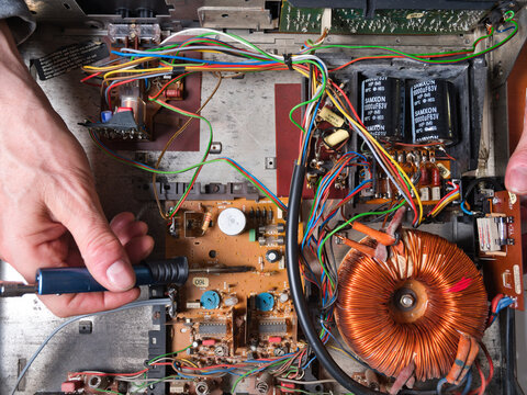 Electronic Device Internal Components - A hand points at the intricate toroidal transformer inside an electronic device, revealing wires, circuits, and capacitors.