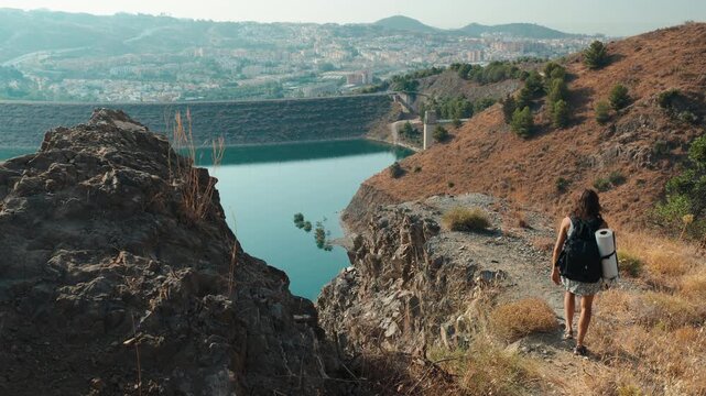 Hiker woman on a cliff overlooking the Embalse de El Limonero dam and reservoir, with Malaga city and the sea in the background, Andalusia, Spain