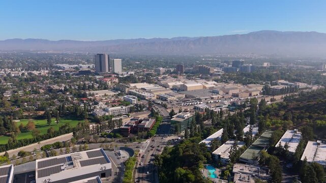 Cinematic aerial view of Warner Brothers Studio in Los Angeles California. Film studio backlot sound stages towers and freeway traffic. Hazy San Gabriel Mountains on sunny summer day.