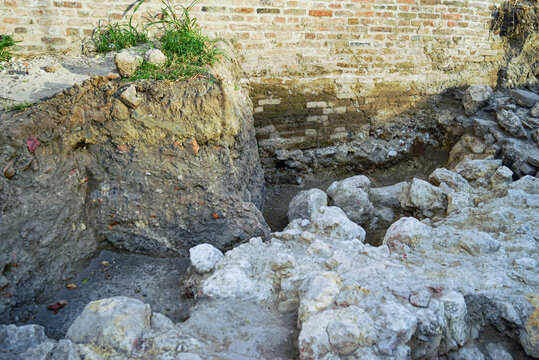 Exposed historic ruins and trench cut into compacted earthen layers beside fortress wall. Reflects stratigraphic excavation, fortification site research, and evidence of successive building phases.