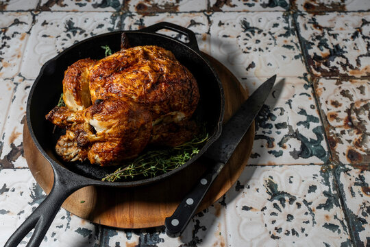 Rotisserie chicken in a cast iron skillet with herbs and a carving knife 