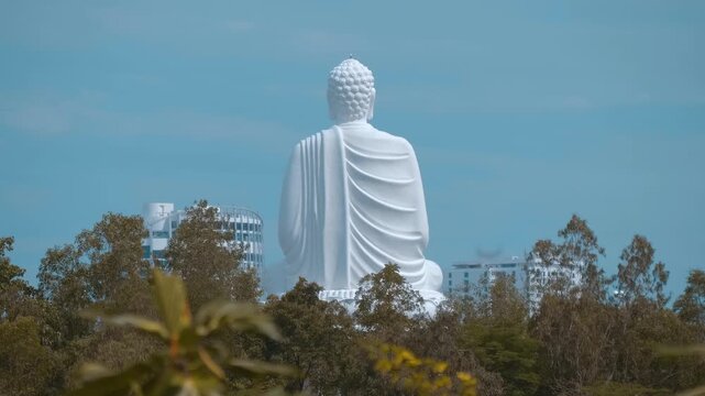 A rear view of the giant white Buddha statue, known as Kim Than Phat To rises above the trees and buildings, located on the top of a hill at the Long Son Pagoda in Nha Trang, Vietnam
