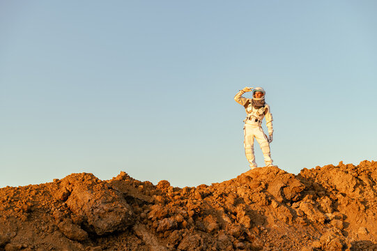 Astronaut standing on the surface of Mars and looking into the distance during daylight