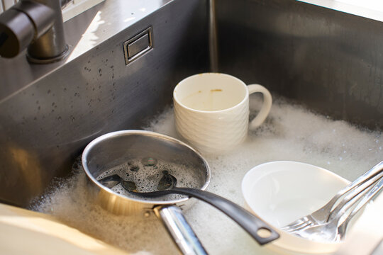 Used cookware and tableware sit in foamy water ready for washing in kitchen sink