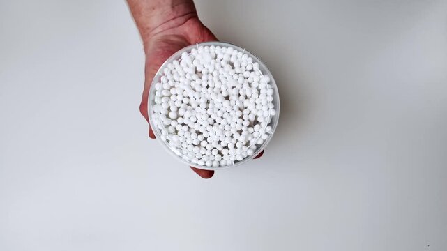a person holds a clear plastic container filled with small white polystyrene foam beads, set against a plain white background