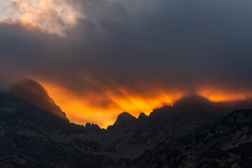 Obraz premium Dramatic Golden Sunbeams Piercing Storm Clouds Over Mountain Peaks at Sunset