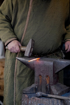 Close-up of a blacksmith holding a hammer over a red hot metal on an anvil, traditional craftsmanship workflow in a forge.