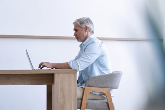 Portrait of happy 40s freelancer man sitting at desk with laptop computer at home office