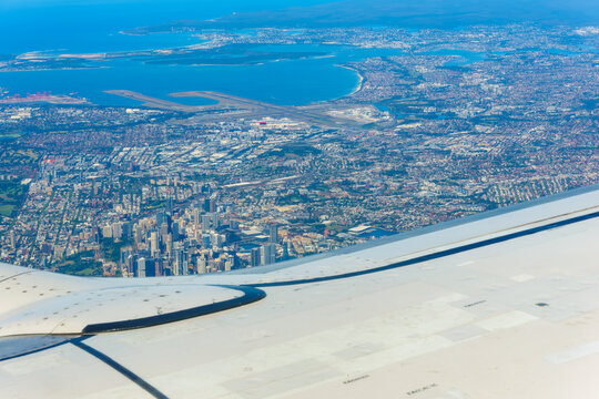View through plane window and over wing while flying into Sydney with business district and sprawling urban area.