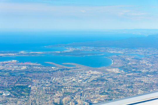 View through plane window and over wing while flying into Sydney with business district and sprawling urban area.