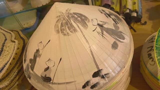 A stack of traditional Vietnamese Non La conical hats, crafted from bamboo and palm leaves features a hand-painted illustration depicting Vietnamese farmers and coconut palms in a rural landscape