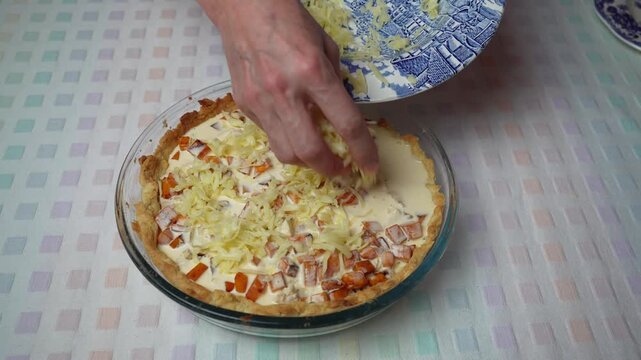 Adding grated cheese to quiche. Hands sprinkle grated cheese over the chicken and pumpkin quiche filling.