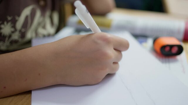 Close-up of a student hand drawing with a white pen on white paper during an art lesson session