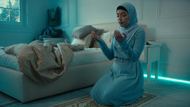 Young Muslim woman in hijab praying on a prayer rug in a serene bedroom