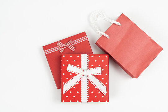 Flat lay of red present boxes with decorative bows next to a paper shopping bag on a white background. Ideal for Christmas, Valentine's Day, and holiday sales