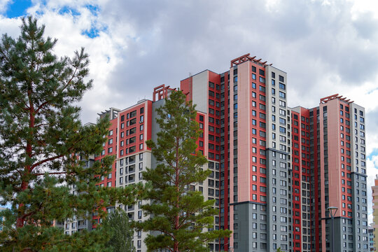 Modern multi-story residential apartment buildings with red and white facade against cloudy sky. Real Photo