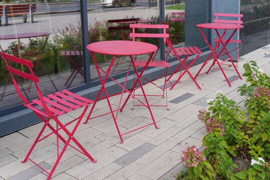 Bright pink metal table and chairs on outdoor cafe terrace on paved street. Restaurant furniture. Real Photo