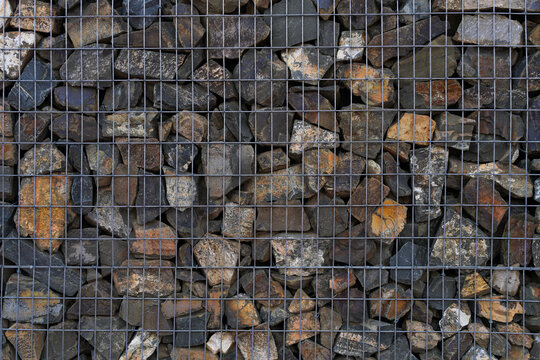 Gabion wall texture filled with various natural stones and held by metal wire grid. Construction material. Real Photo