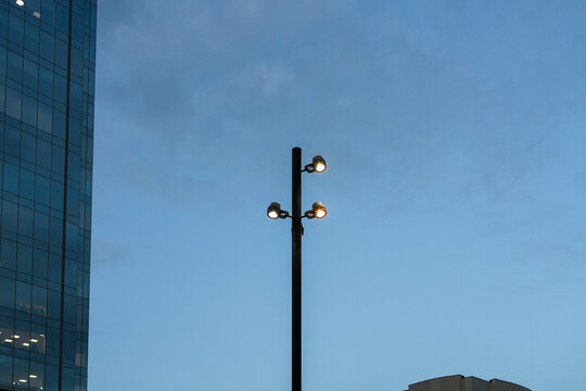 Modern black street lamp post with triple globe lights against blue evening sky. Urban lighting. Real Photo
