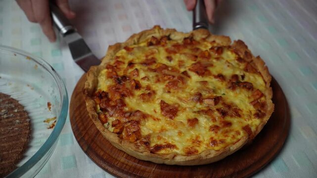 Removing quiche from the baking dish. Hands transfer the baked quiche from its round baking dish onto a wooden board.
