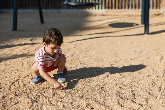 Young child drawing playing in sand playground