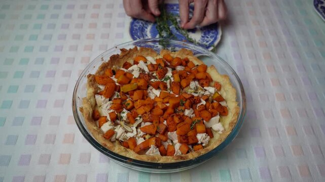 Adding thyme to the quiche filling. Hands sprinkle fresh thyme over the chicken and pumpkin filling.