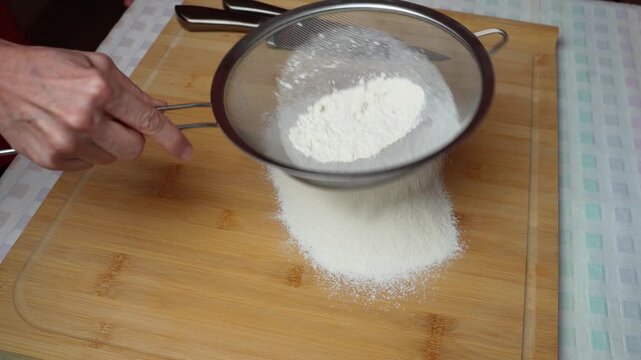 Sifting flour on a wooden board. Hands sift flour onto a wooden work surface to prepare pastry dough.