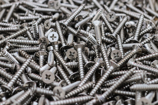 Close up of a large pile of new stainless steel screws with cross recess countersunk heads and sharp coarse threads, a metal fastener background for construction and hardware supply.