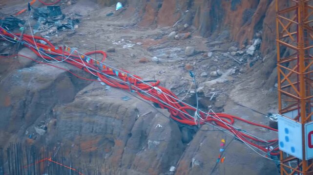 Orange tower crane structural mast standing on the construction site with bundles of flexible red corrugated plastic tubes/pipes used to protect underground electrical, power, or communication cables