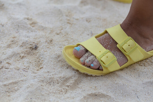 Yellow sandal with blue painted nails on a white sand beach
