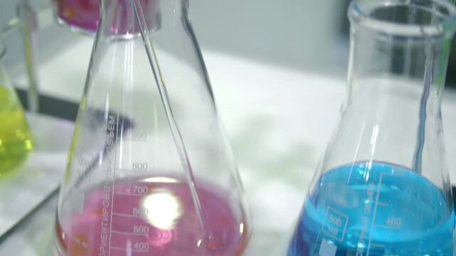 On the laboratory table are several flasks with multi-colored solutions, ready for further reactions in the process of scientific research. Closeup. Shot in motion. Follow focus